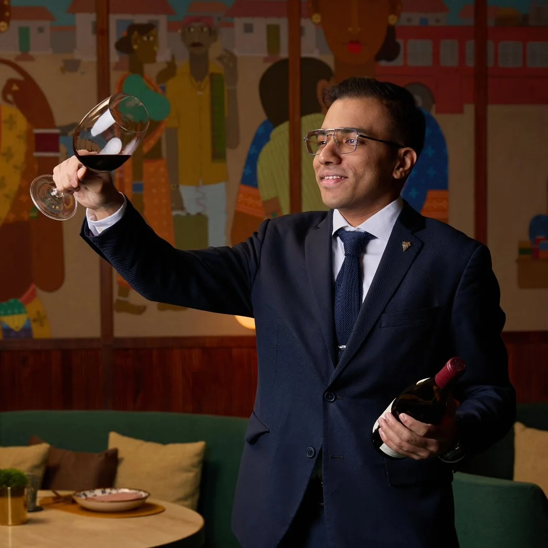 Amit examining a glass of red wine while holding a bottle